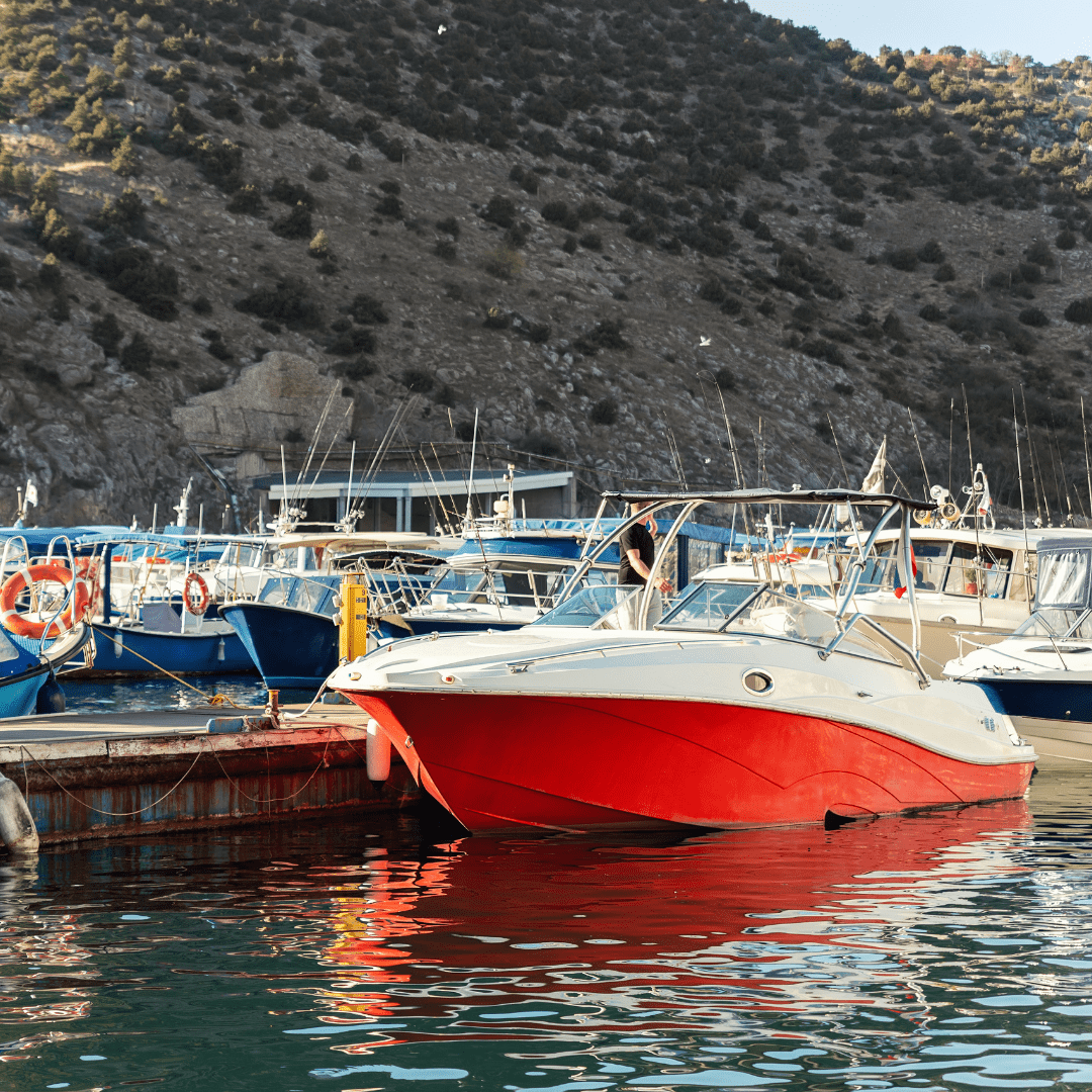 A red and white renting speedboat docked in a marina with other boats, surrounded by scenic mountains.