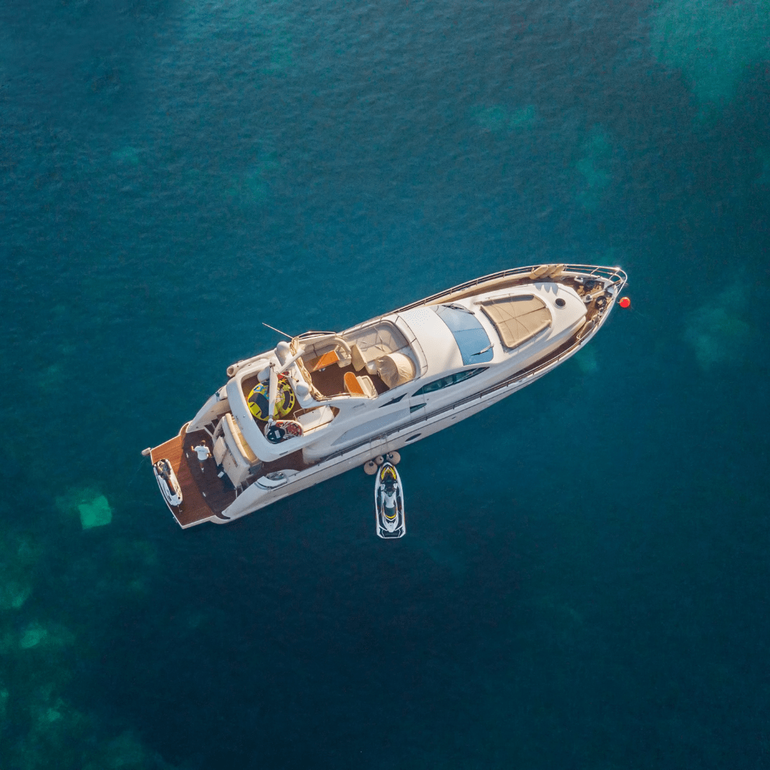 Aerial view of a luxury Boat Rental anchored in crystal-clear waters with jet skis floating nearby.